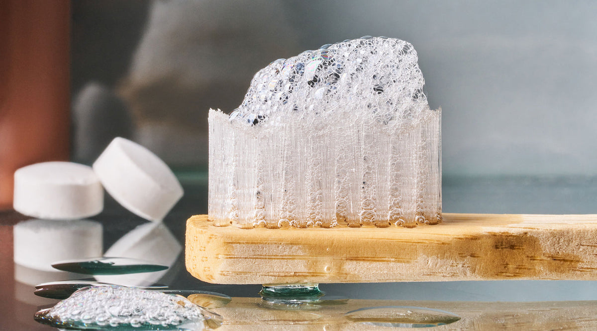 Toothbrush with foam on it with Huppy Toothpaste tablets in the background.