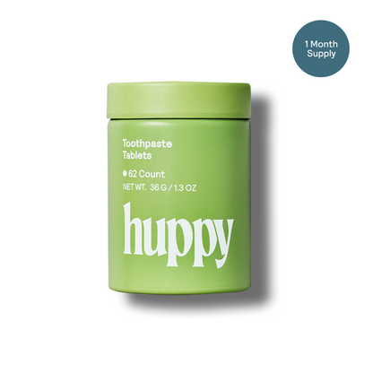 Green container of Huppy peppermint toothpaste tablets on a white background