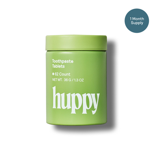 Green container of Huppy peppermint toothpaste tablets on a white background