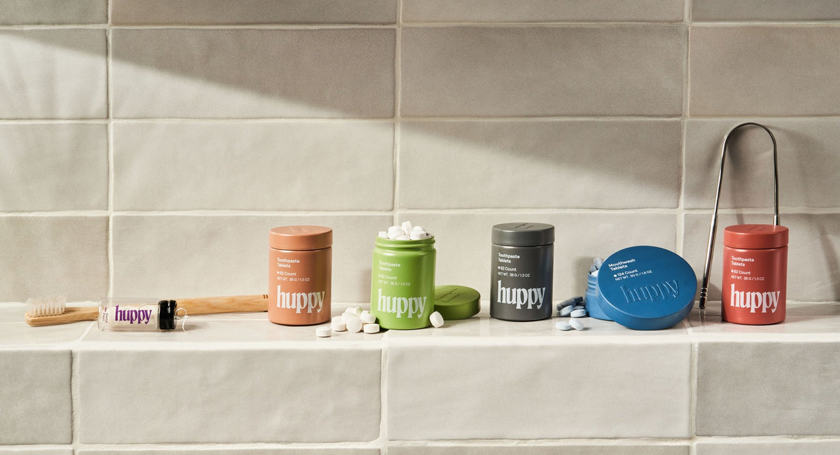 Huppy toothpaste tablets, mouthwash tablets, floss, toothbrush and tongue cleaner on a bathroom shelf